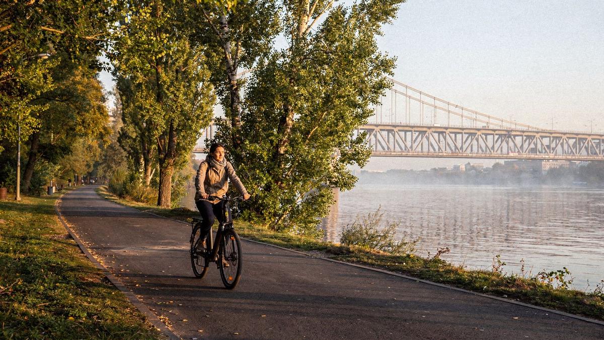 Cyclist on a riverside path in Kyiv with a bridge behind